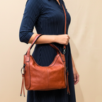 Person holding a brown leather handbag against a beige background
