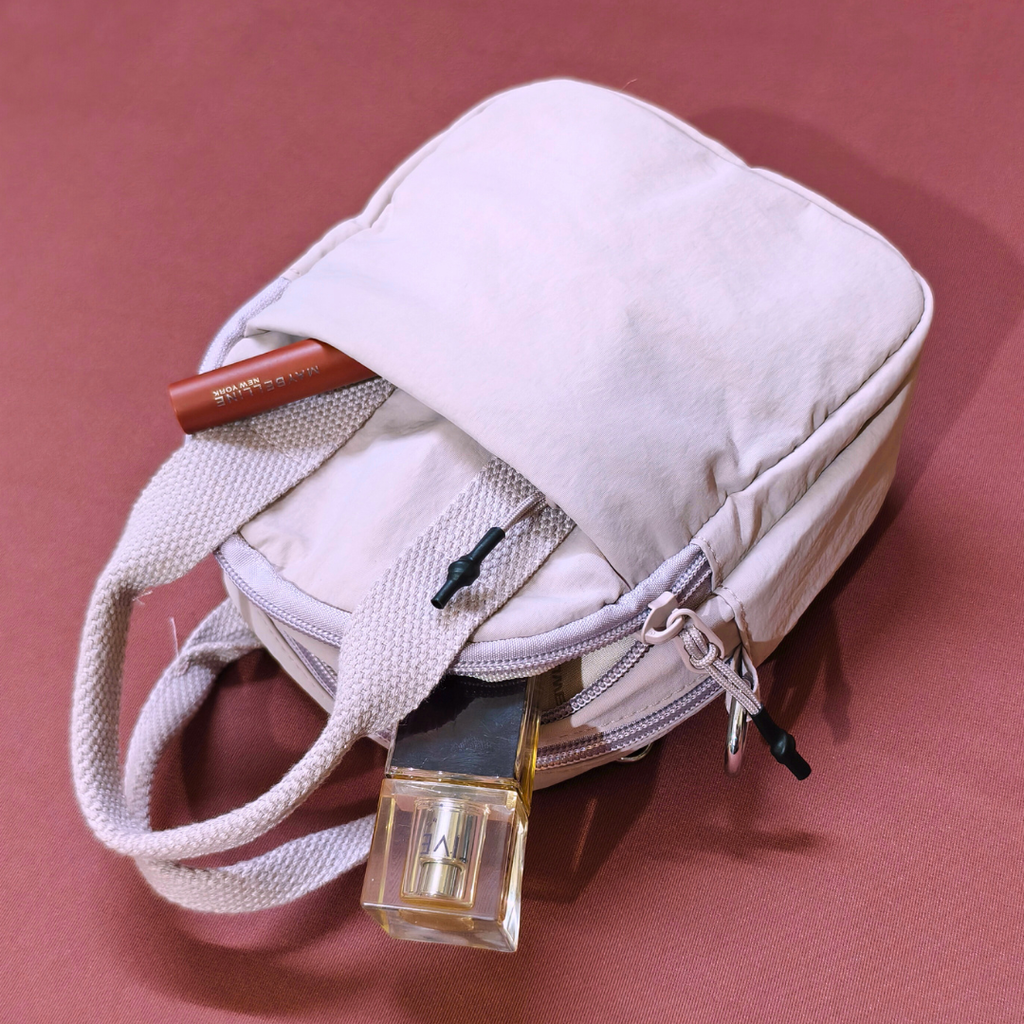 Beige handbag with makeup items on a pink background