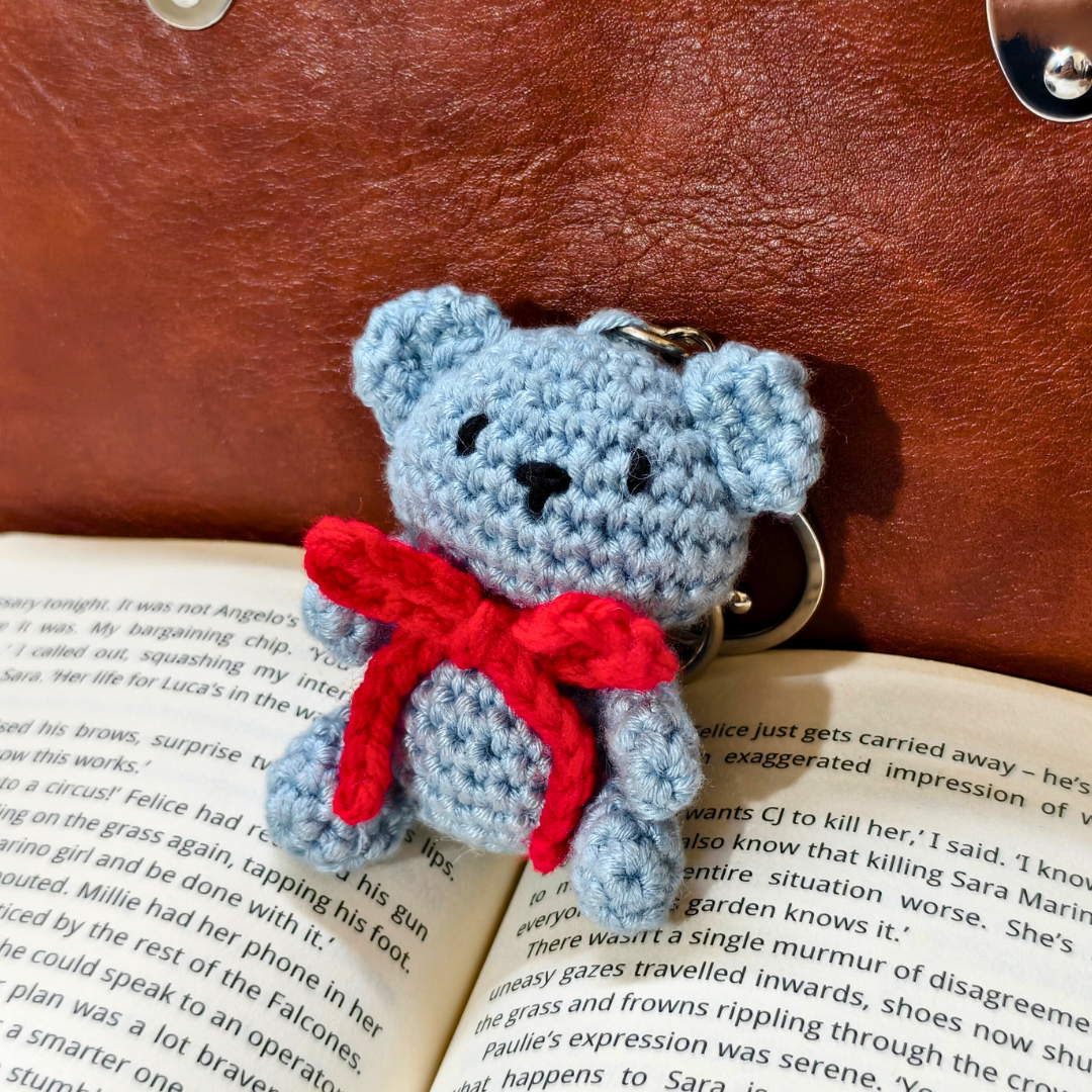 Blue teddy bear keychain with a red bow on an open book