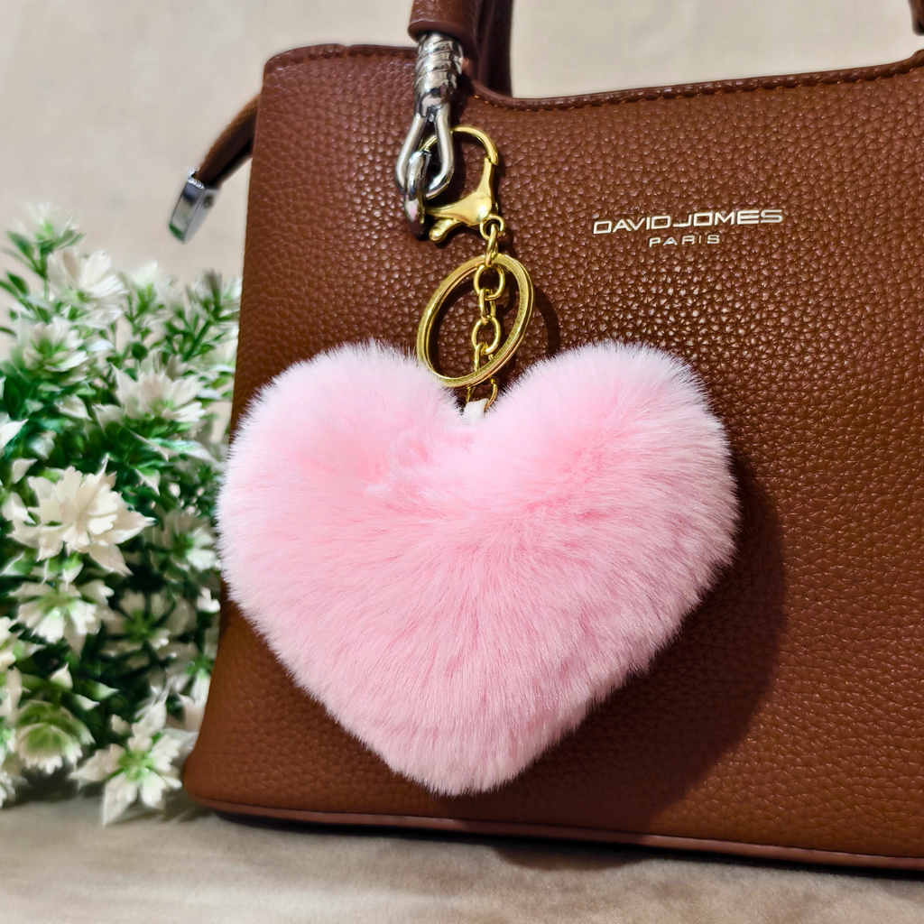 Pink heart-shaped fluffy keychain on a brown handbag with 'David Jones' branding, next to green plants.