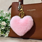 Pink heart-shaped fluffy keychain on a brown handbag with 'David Jones' branding, next to green plants.