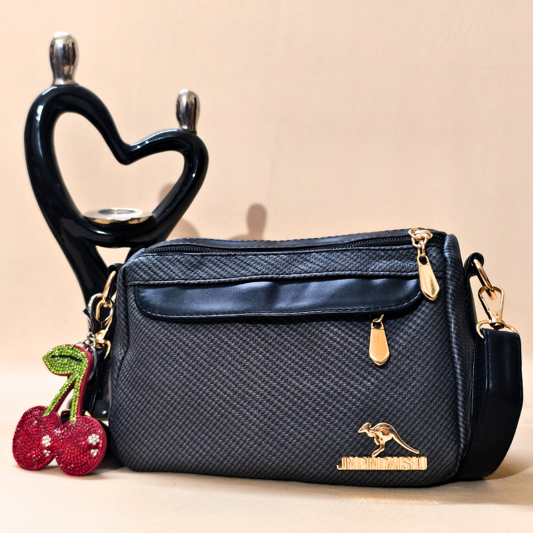Black handbag with gold accents and cherry charm on a beige background