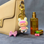Keychain with cartoon character attached to a handbag next to a bottle of perfume on a gray surface.