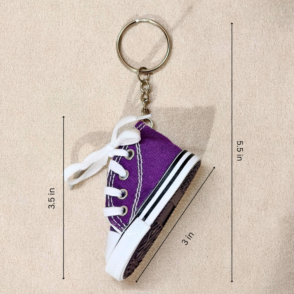 Purple canvas sneaker keychain with white laces and a silver metal key ring, shown on a beige textured background with dimension lines and text indicating measurements of 3.5 in height, 5.