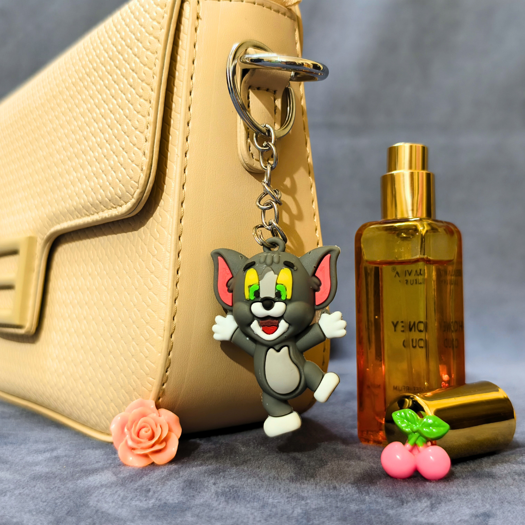 Cartoon cat keychain attached to a beige handbag with a bottle of perfume next to it.