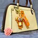 Beige handbag with a cartoon character keychain and pink flower on a gray background