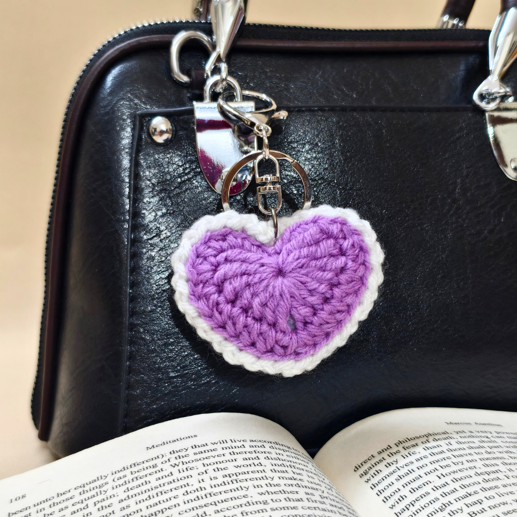 Purple heart-shaped keychain on a black handbag with an open book underneath