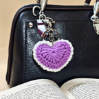 Purple heart-shaped keychain on a black handbag with an open book underneath