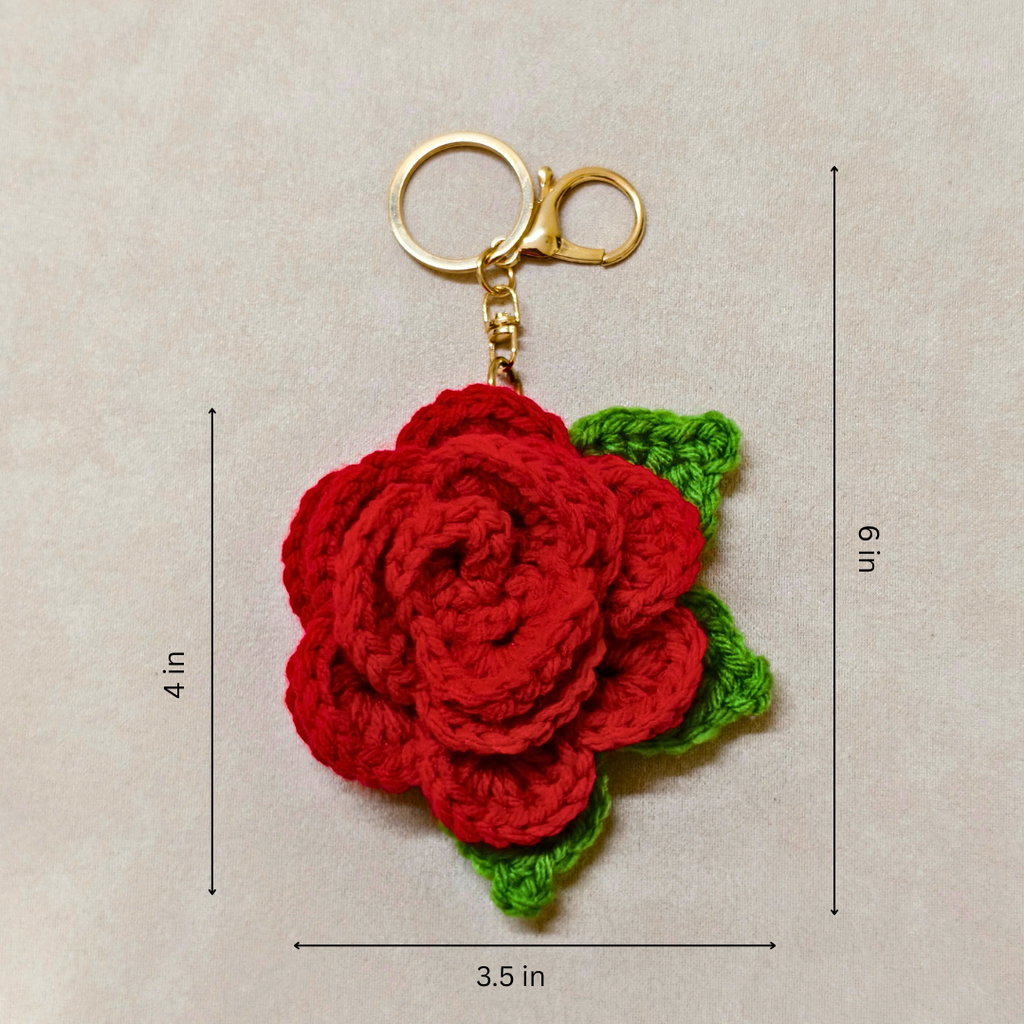 Crocheted red rose keychain with green leaves on a beige background, showing measurements.