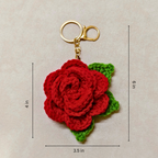 Crocheted red rose keychain with green leaves on a beige background, showing measurements.