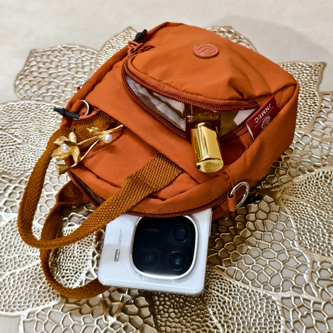 Orange crossbody bag with a phone and items on a textured surface