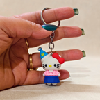 Hand holding a keychain with a cartoon character wearing a blue hat and pink dress.