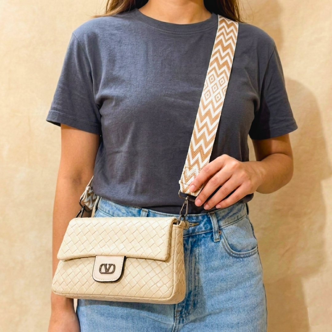 Person wearing a blue t-shirt and jeans with a beige handbag and patterned strap.
