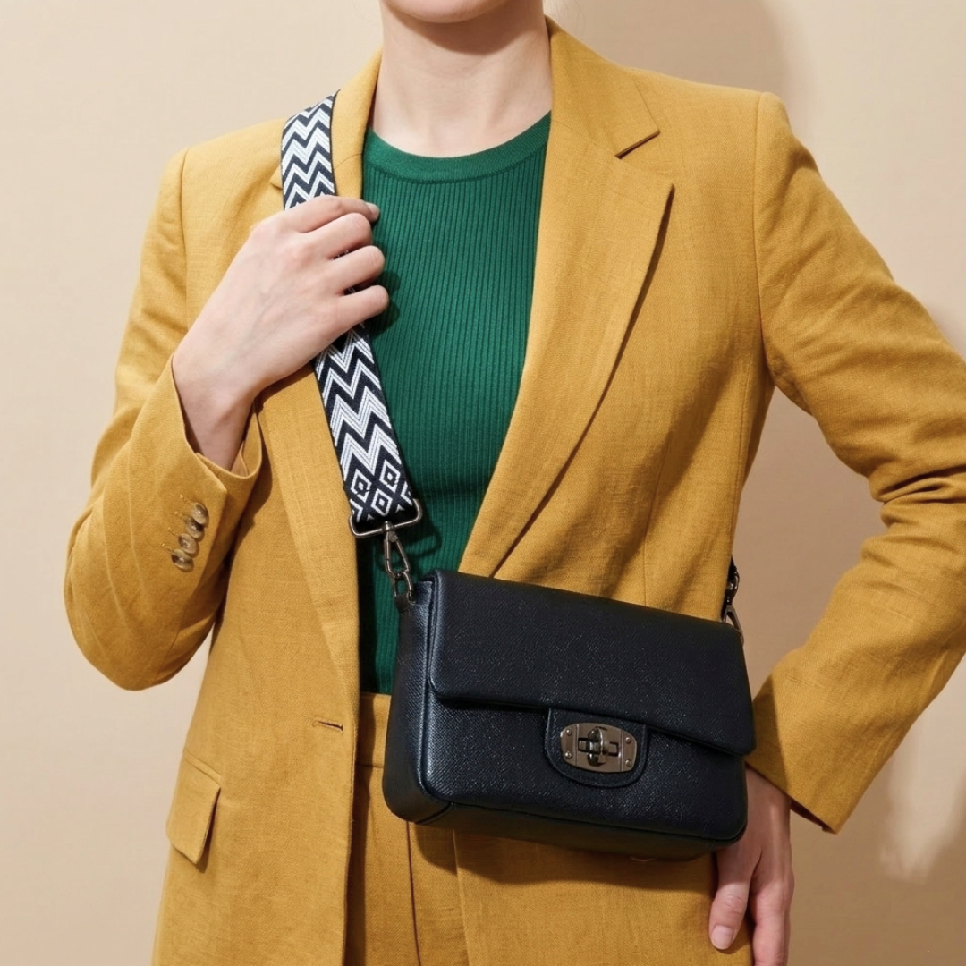Person wearing a mustard yellow blazer with a black handbag and green sweater against a beige background