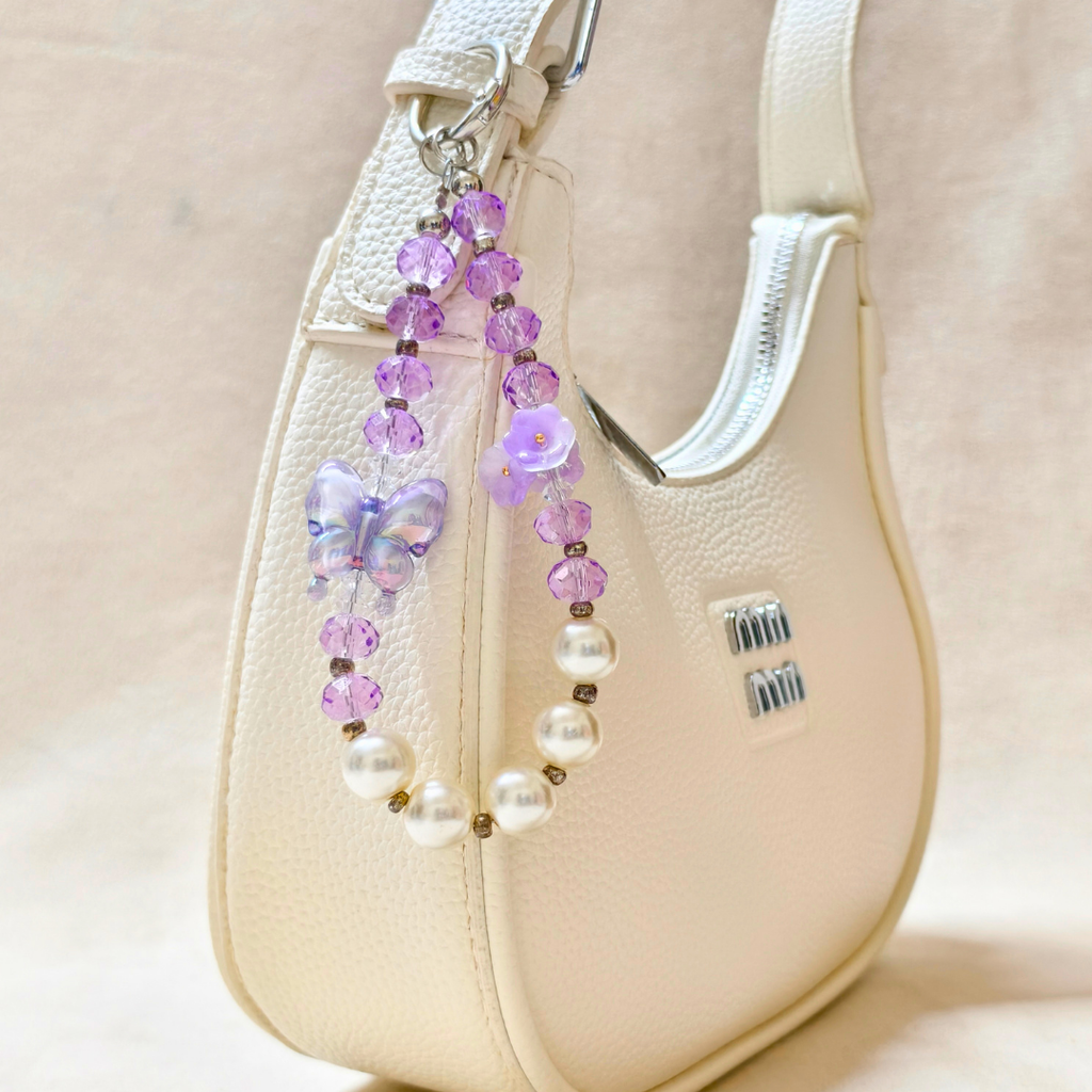 Beaded strap with purple and white beads on a beige handbag.