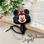A black Minnie Mouse-themed phone stand with a red polka-dot bow and Mickey face, placed on an open book with decorative flowers and a branch in the background.