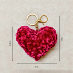 Pink heart-shaped keychain with gold clasp on a beige background with measurements.