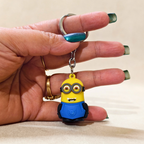 Hand holding a keychain shaped like a yellow character with blue overalls.