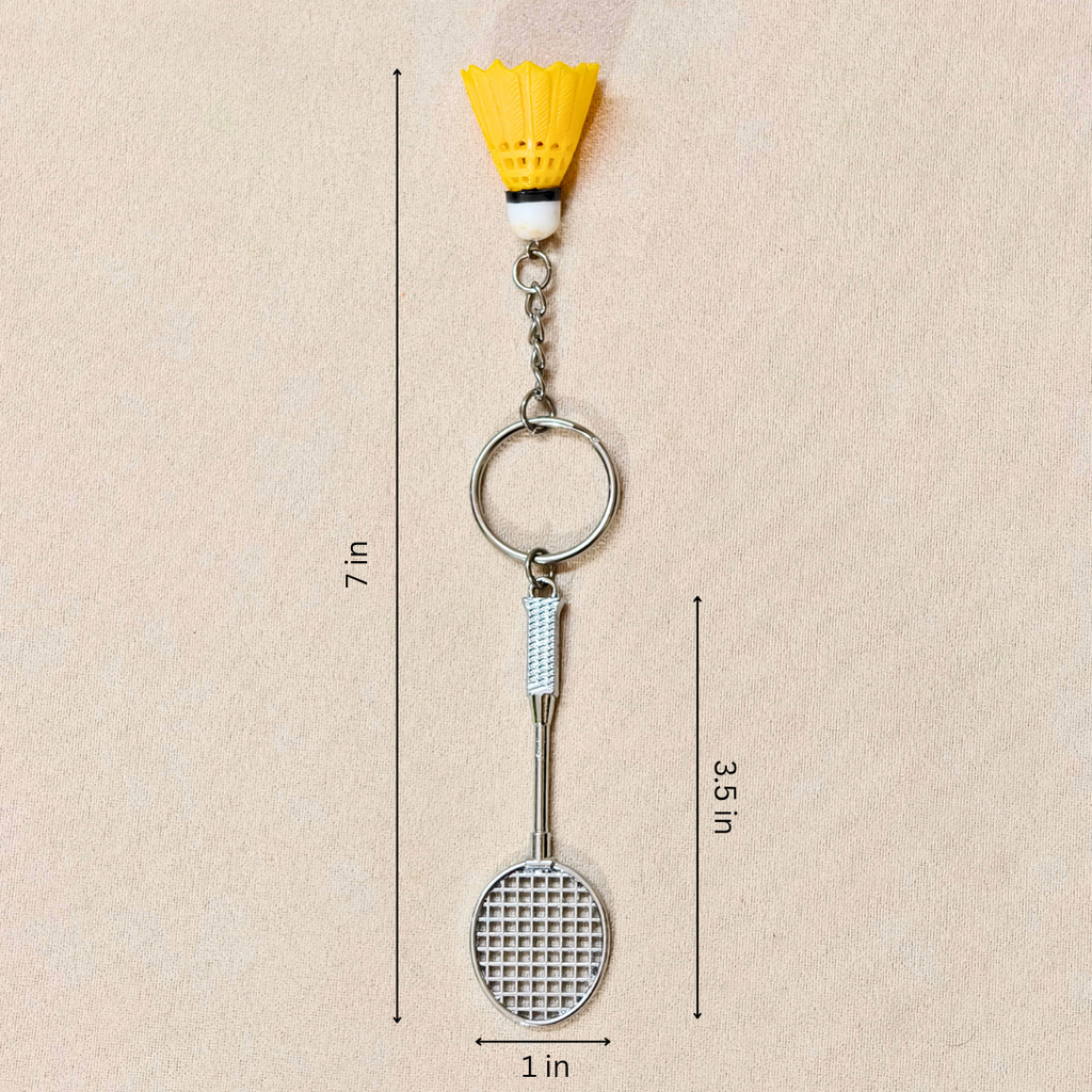 silver metal badminton racket keychain with a small pink and white plastic shuttlecock attached, showing measurements against a plain beige background.


