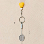 silver metal badminton racket keychain with a small pink and white plastic shuttlecock attached, showing measurements against a plain beige background.


