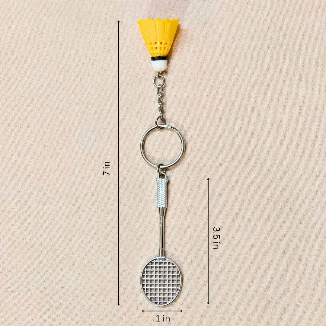 silver metal badminton racket keychain with a small pink and white plastic shuttlecock attached, showing measurements against a plain beige background.


