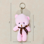 A pink plush teddy bear keychain with a brown ribbon and metal key ring, shown on a light beige background with dimension lines indicating 7 in height, 4 in width, and 3 in depth.