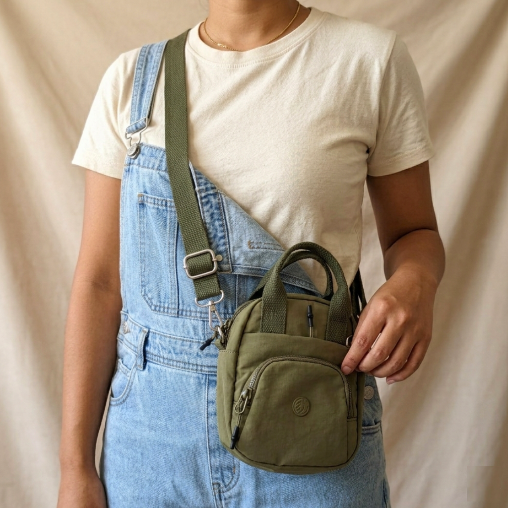 Person wearing blue overalls and a white shirt holding a green bag against a beige background