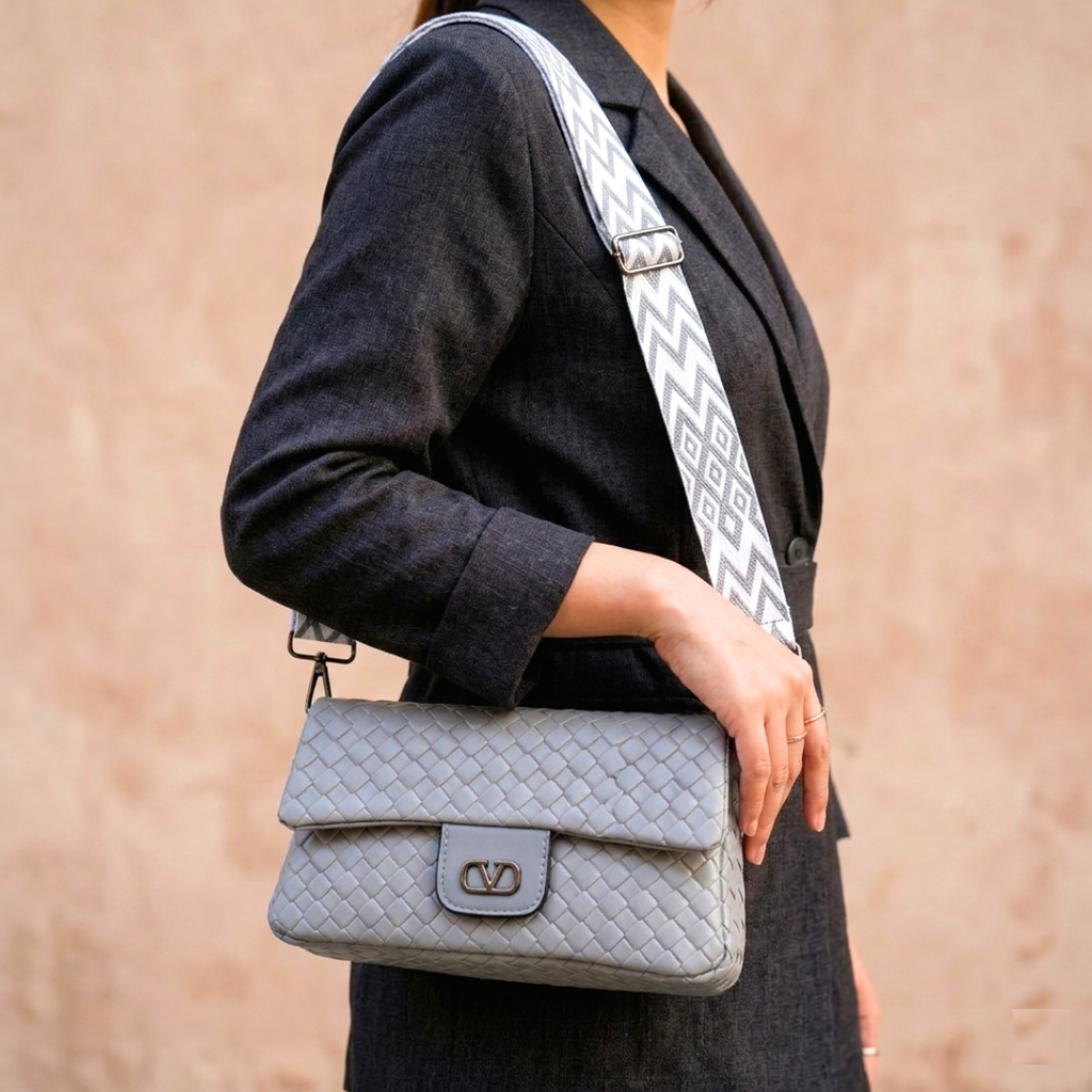 Person holding a gray handbag with a patterned strap against a beige background