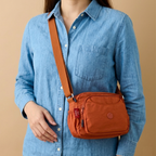 Model Carrying Rust Brown Sling Bag  In Front Of Beige Background.