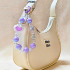 Beige handbag with a decorative beaded strap featuring purple and pink beads.