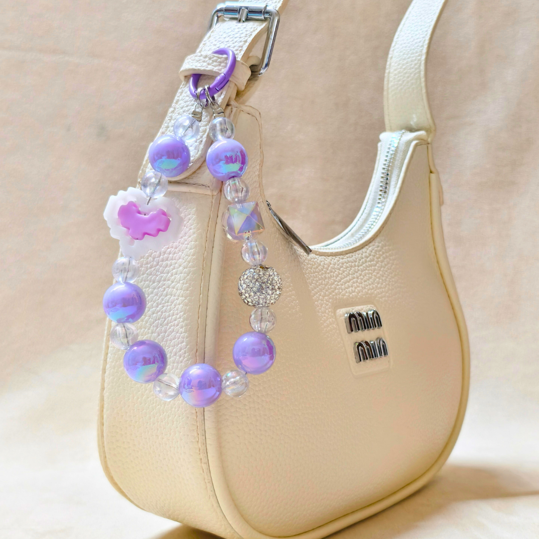 Beige handbag with a decorative beaded strap featuring purple and pink beads.