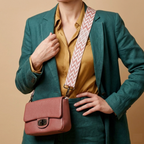 Person wearing a green blazer and mustard shirt with a pink handbag and patterned strap on a beige background