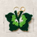 Green butterfly-shaped keychain with measurements on a beige background