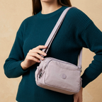 Model Carrying Lavender Lilac Sling Bag In Front Of Beige Background.