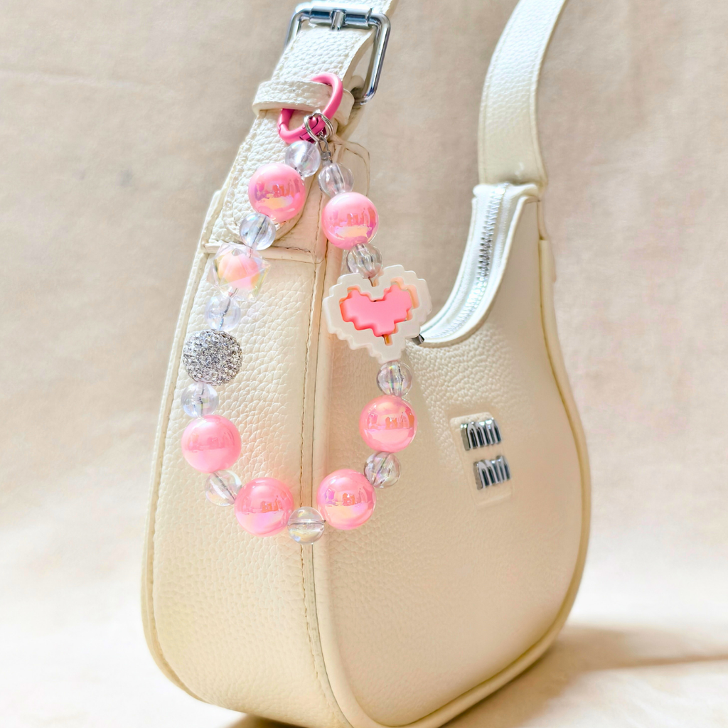 Beaded handbag charm with pink beads and heart-shaped clasp on a beige handbag.