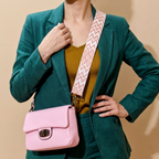 Person wearing a green blazer with a pink handbag and patterned strap on a beige background