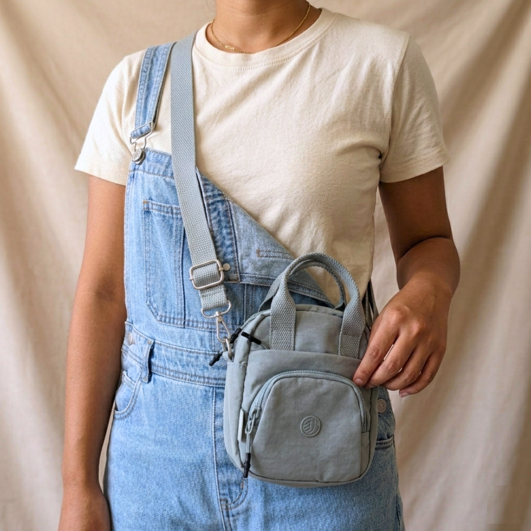 Person wearing blue overalls holding a matching blue bag against a beige background