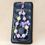 Lilac Bow Charm Attached To Phone In The Front Of Beige Background.