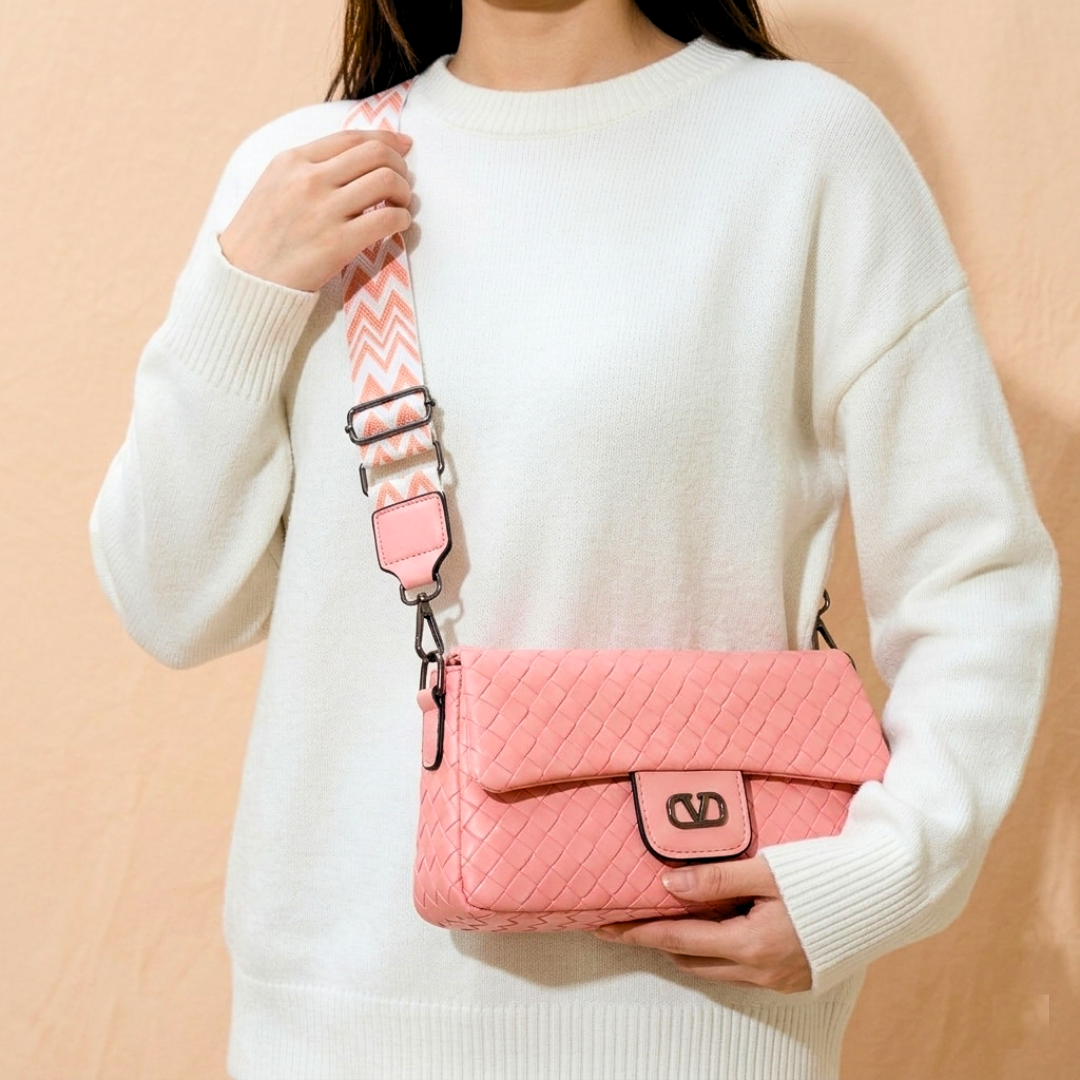 Person holding a pink quilted handbag with a patterned strap against a beige background