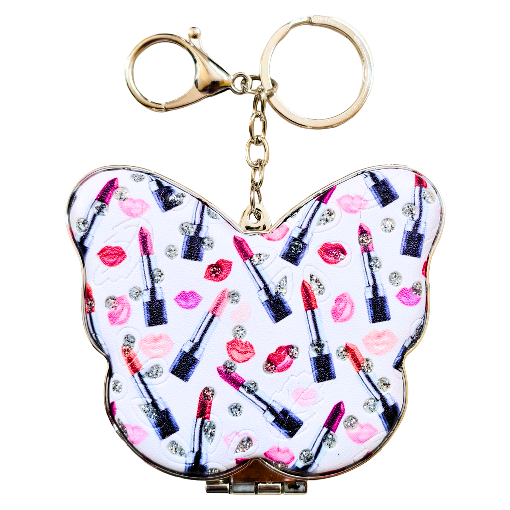 A butterfly-shaped compact mirror keychain featuring a white background printed with pink lip prints, red and pink lipsticks, and rhinestone accents, complete with a gold-tone clasp and key ring.