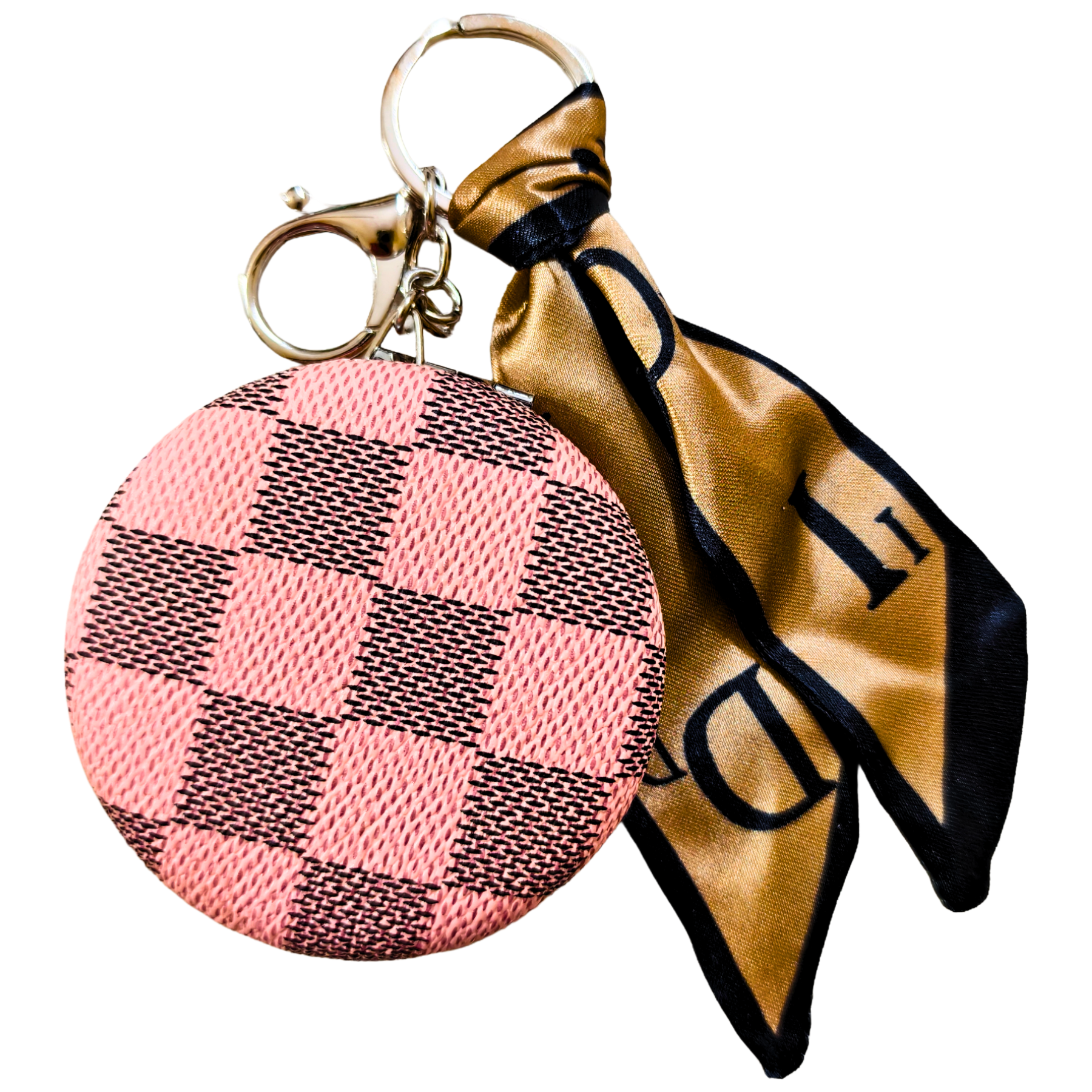 A circular coin purse keychain with a pink and black checkered pattern, attached to a gold-tone key ring and a gold satin necktie with black trim and lettering.