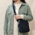 Person wearing a green jacket with a black crossbody bag on a beige background