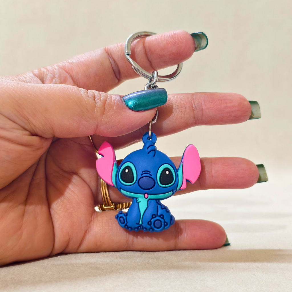 Hand holding a blue cartoon character keychain with pink accents on a beige background