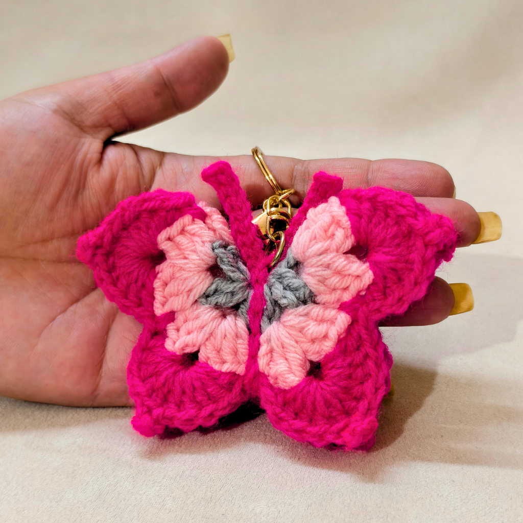 Hand holding a pink and gray butterfly-shaped crochet keychain.