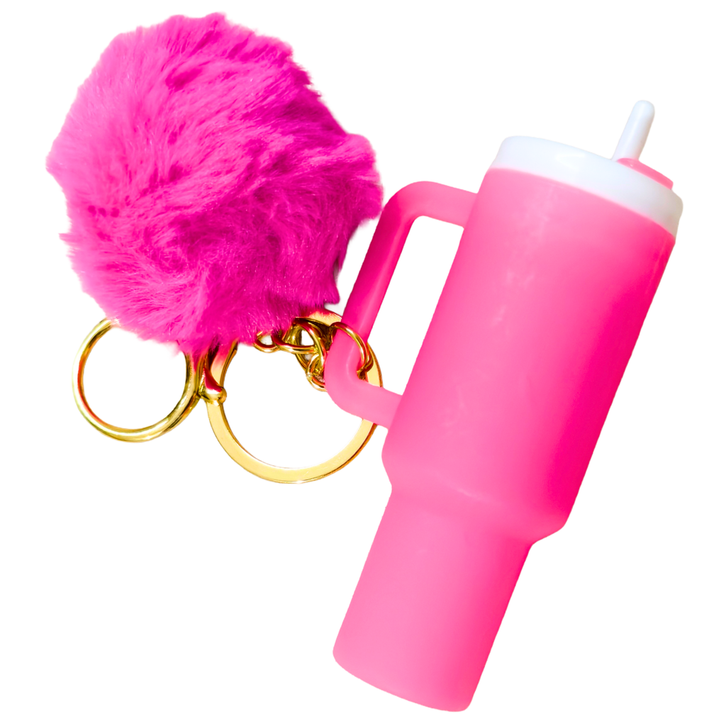 A bright pink silicone tumbler keychain with a matching pink faux fur pom-pom, gold split rings, and a white lid, shown on a plain white background.