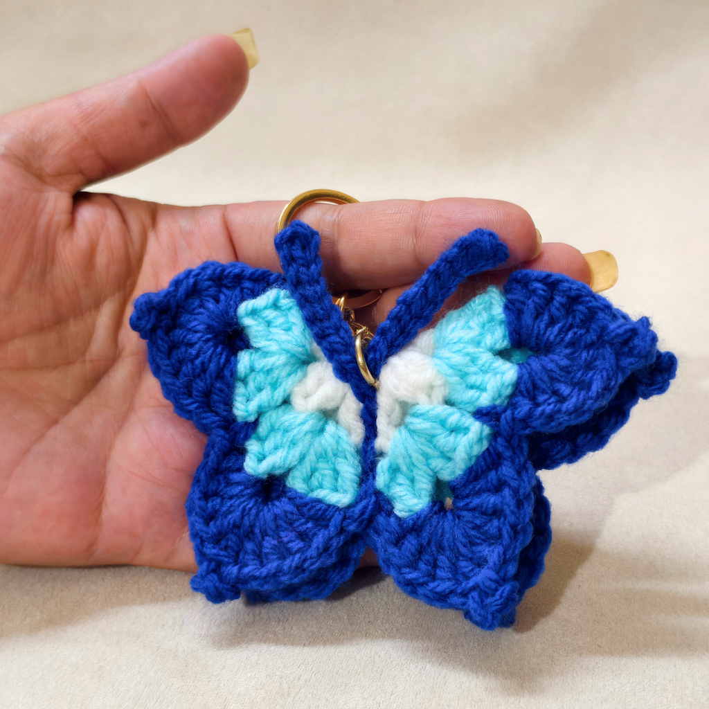 Hand holding a blue and turquoise crocheted butterfly keychain.