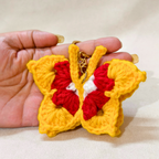 Hand holding a yellow and red butterfly-shaped keychain against a neutral background