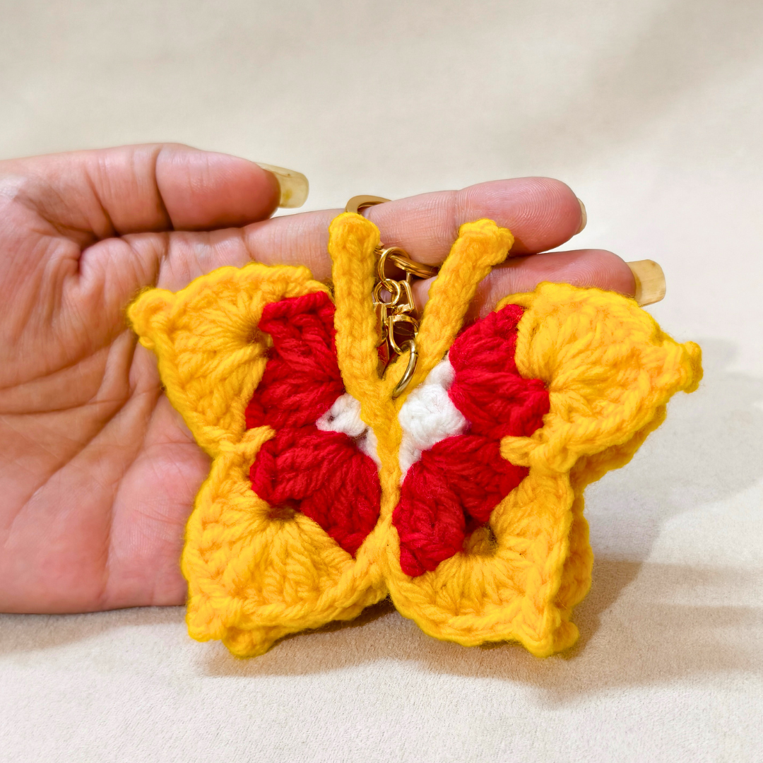 Hand holding a yellow and red butterfly-shaped keychain against a neutral background