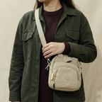 Person wearing a green jacket with a beige crossbody bag on a neutral background