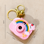 Pink camera-shaped keychain with rainbow design and measurements on a beige background